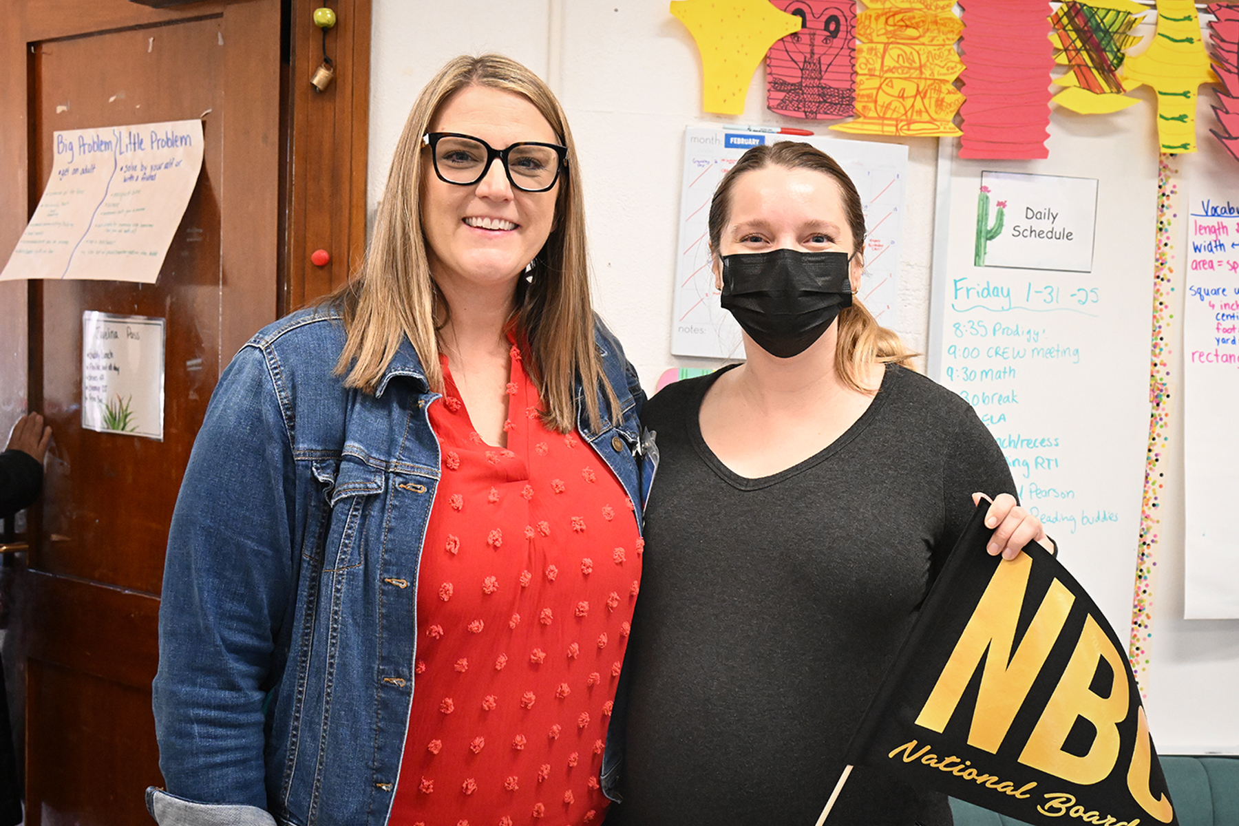 A woman in glasses smiles next to a woman in a face mask