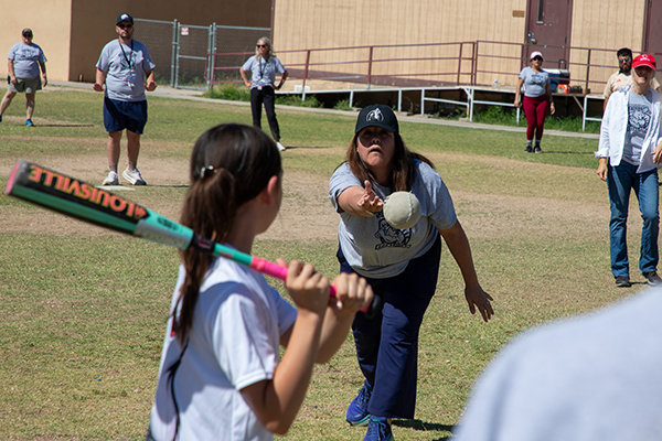 A woman throws out a softball as a girl stands at the plate, bat ready to swing