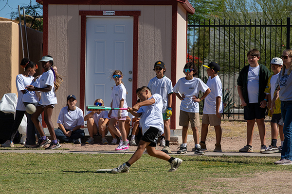 A boy goes in to swing the bat at the softball